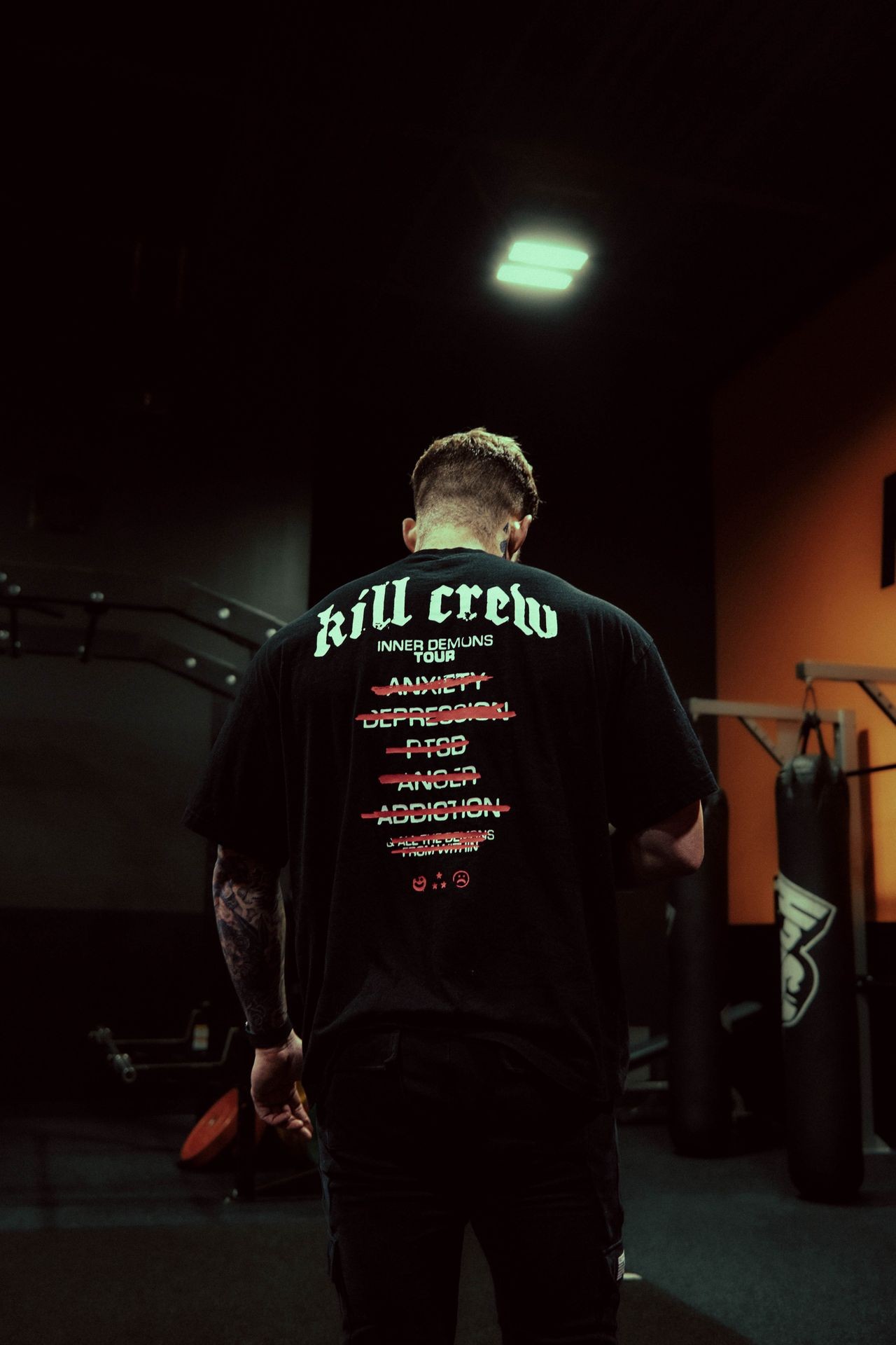 Man in gym wearing a black T-shirt with motivational text and punching bags in the background.